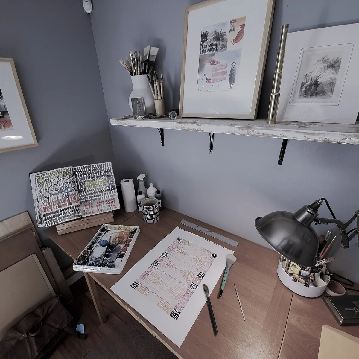 Werktafel in een thuisatelier met kwasten, verf, schetsboek en een aquarel in bewerking